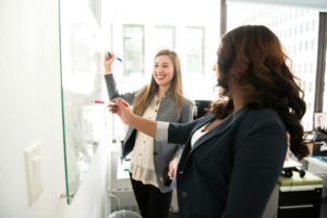 WORKPLACE, Two professional women discussing ideas on a whiteboard in a modern office setting.