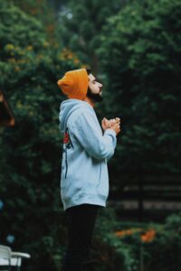 breath, A man in a beanie and hoodie deeply praying outside in a lush green forest.