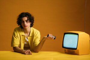 Young man in yellow with a vintage TV in a cool, retro setting.