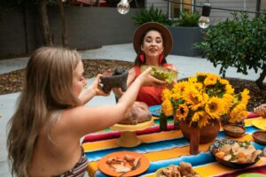 Two women sharing a vibrant Mexican meal outdoors with colorful decor and sunflowers.